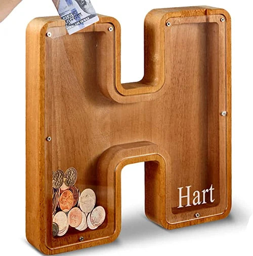 "Barn håller träbokstavs-spargris med glaspanel och bokstavsdesign, perfekt för pedagogisk sparning och inredning."