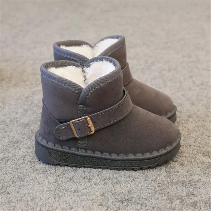 Pojke i röda vinterkängor, lekandes i snön. Varma, vattentäta, perfekta snöskor för barn utomhus.