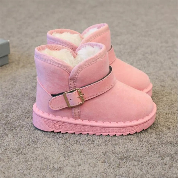 Flicka i rosa barnkängor med mjukt plyschfoder, ler och kastar snöboll. Mysiga snöskor för flickor.