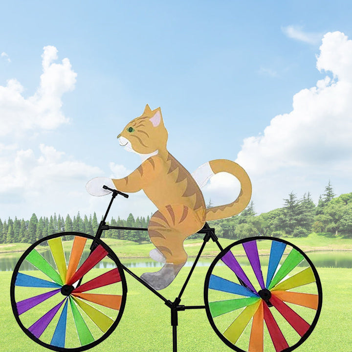 "Charmig katt på cykel vindsnurra, regnbågseffekt, färgglad trädgårdsdekoration, glittrande tygremsor i rörelse."