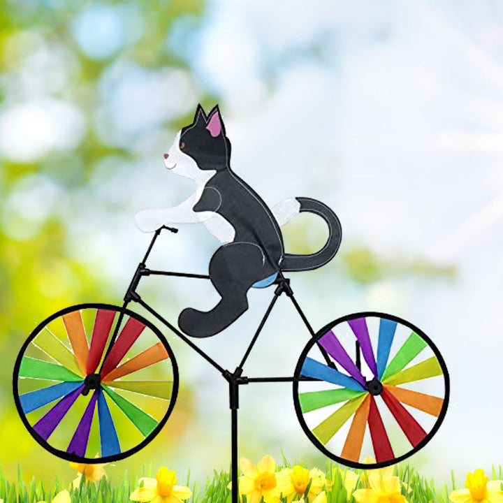 "Charmig katt på cykel vindsnurra, regnbågseffekt, färgglad trädgårdsdekoration, glittrande tygremsor i rörelse."