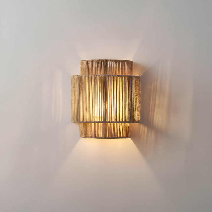 "Elegant boho hampavägglampa med rottingdetaljer, handgjord design som ger ett lugnande sken och naturlig atmosfär."