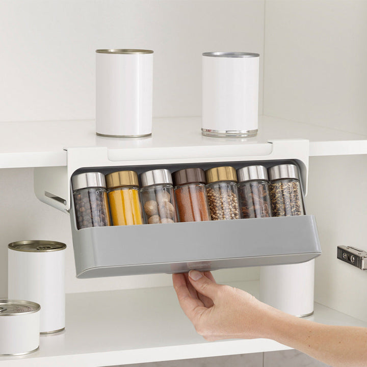 "Kryddorganisatör under hyllan med vit plastdesign, plats för sju kryddburkar, enkel installation i köket."