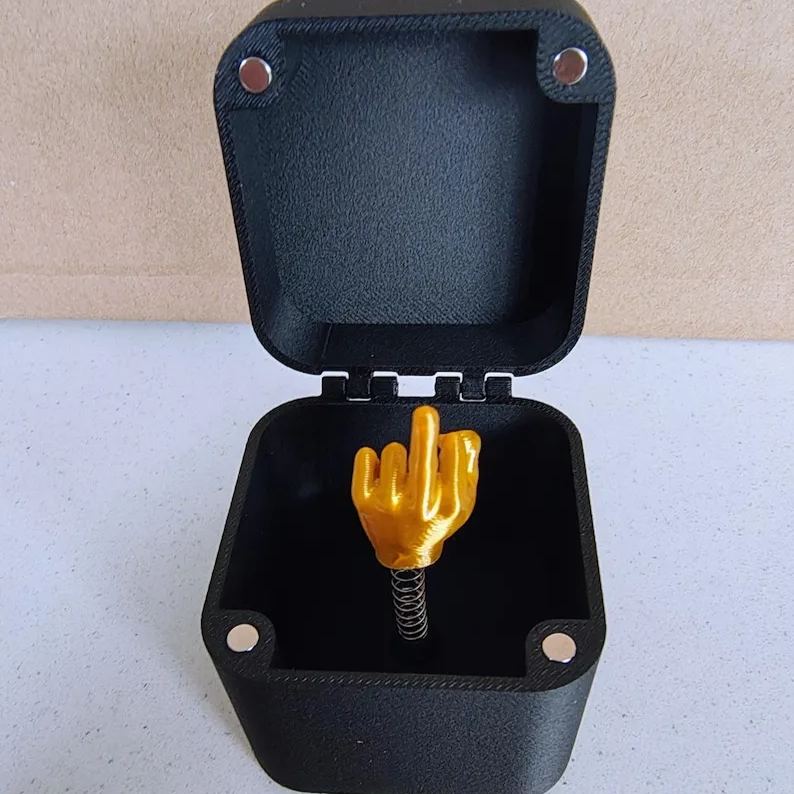 "Långfingret i en svart dosa med gulddetaljer, humoristisk present för honom och henne, hållbar PLA-plast, skämtsamma accesso