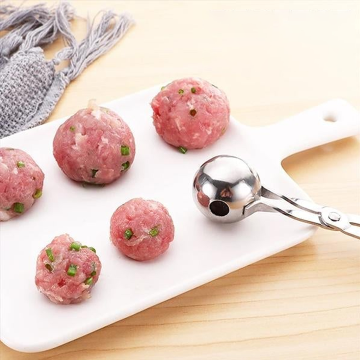 "Rostfri köttbulleskopa i silver, saxgrepp-design, idealisk för jämna köttbullar, meloner och kakbollar, i köksmiljö."