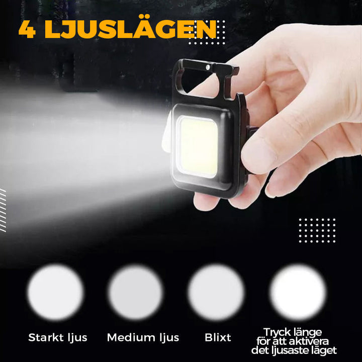 "Svart multifunktionell nyckelring nödljus med kompakt design och 4 ljuslägen, perfekt för utomhusaktiviteter."